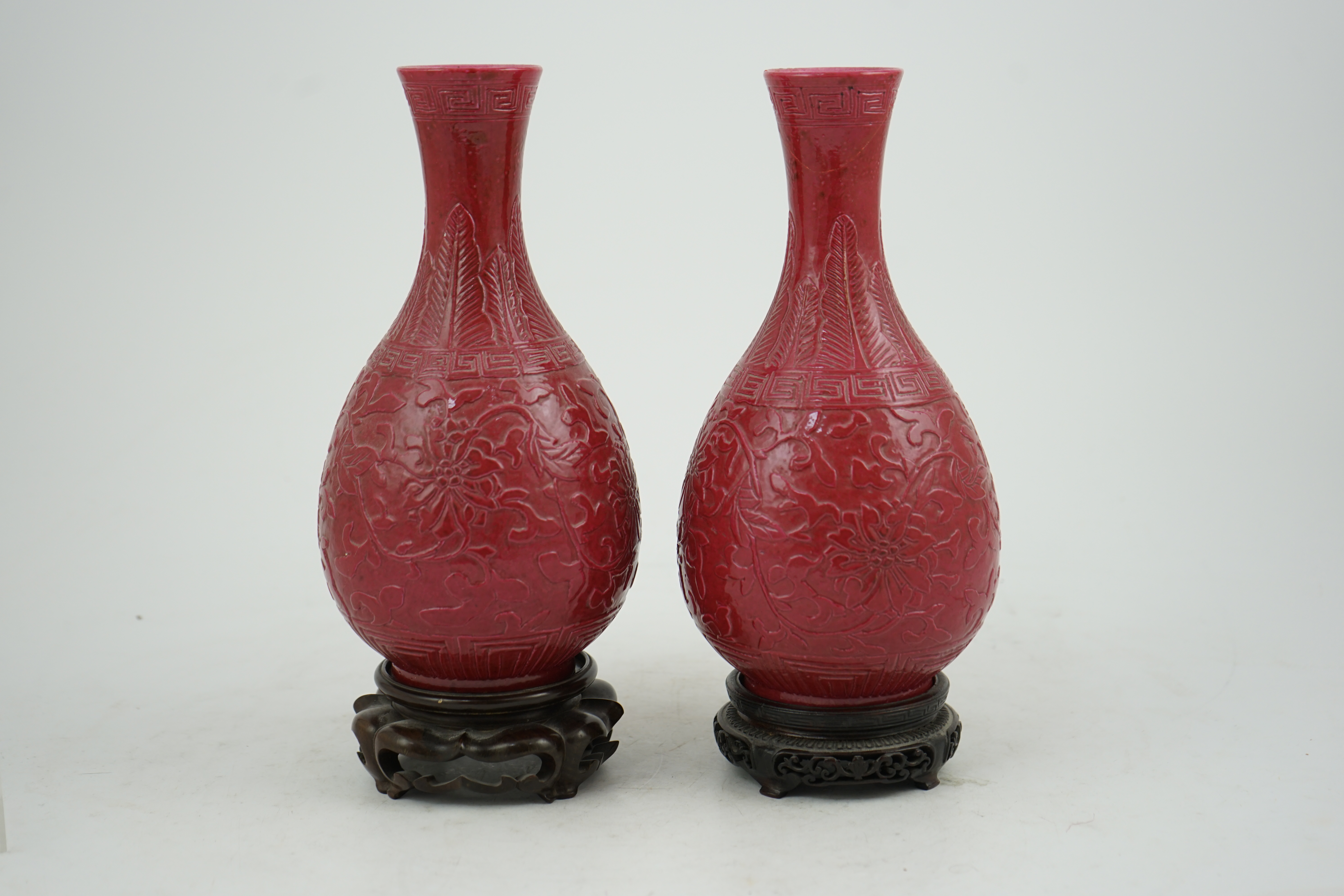 A pair of Chinese ruby ground ‘lotus’ bottle vases, late 19th century, each carved in relief with lotus flowers, scrolling tendrils and leaves, both with carved stands, 24cm high. Condition - one vase the neck broken bot